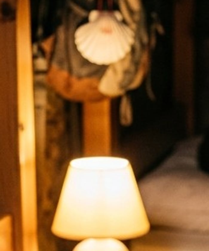 A backpack with a scallop shell hanging above a warm bedside lamp