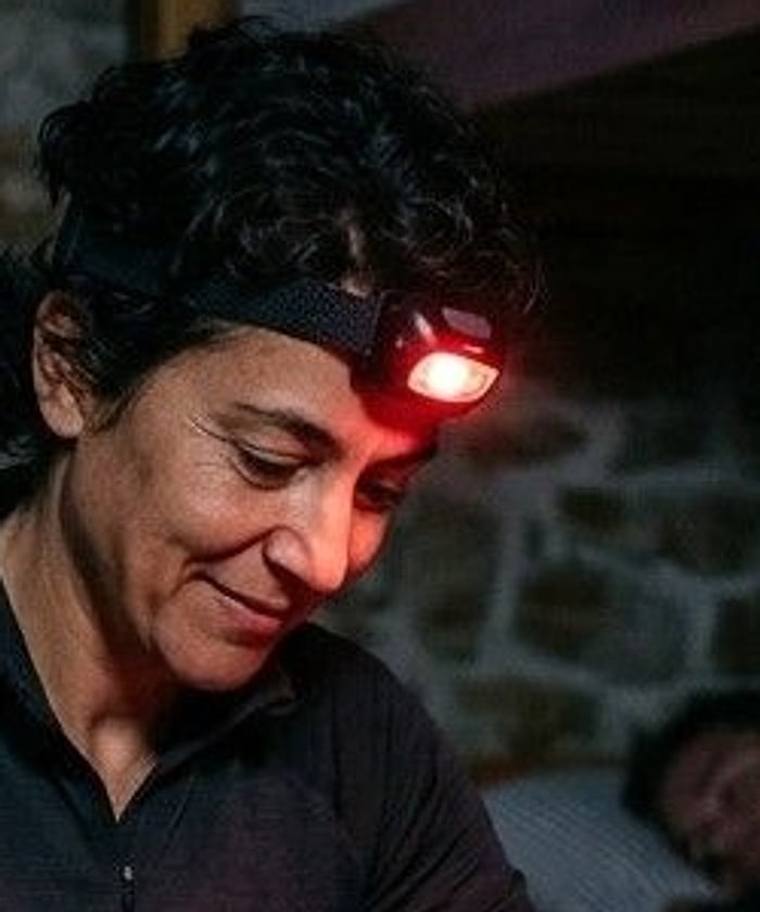 A pilgrim with short dark curls wearing a small headlamp glowing red