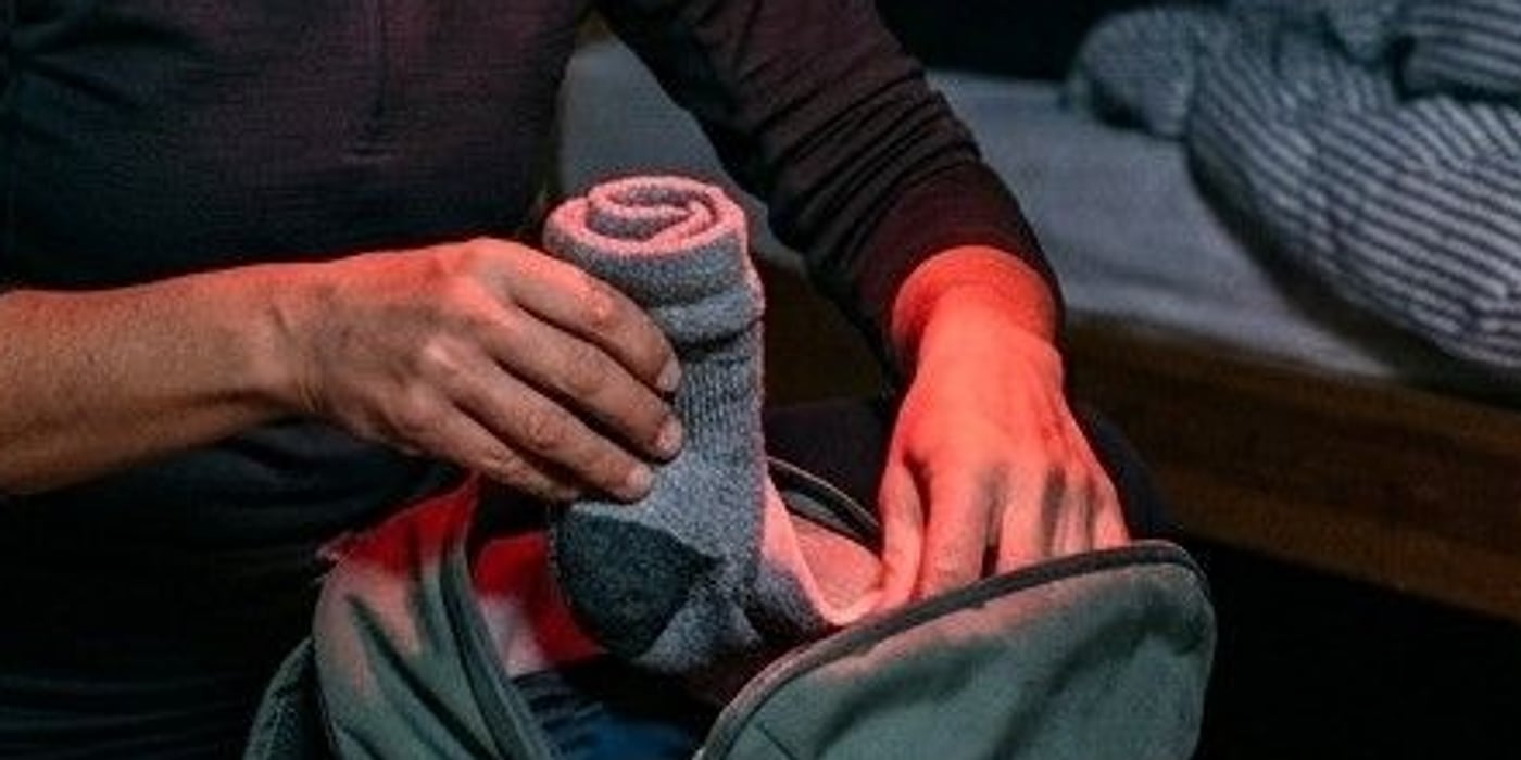 Close-up of hands lit red, tucking rolled socks into a backpack