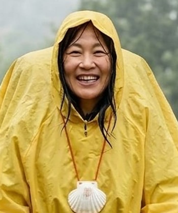 A delighted pilgrim under a yellow hood in the rain